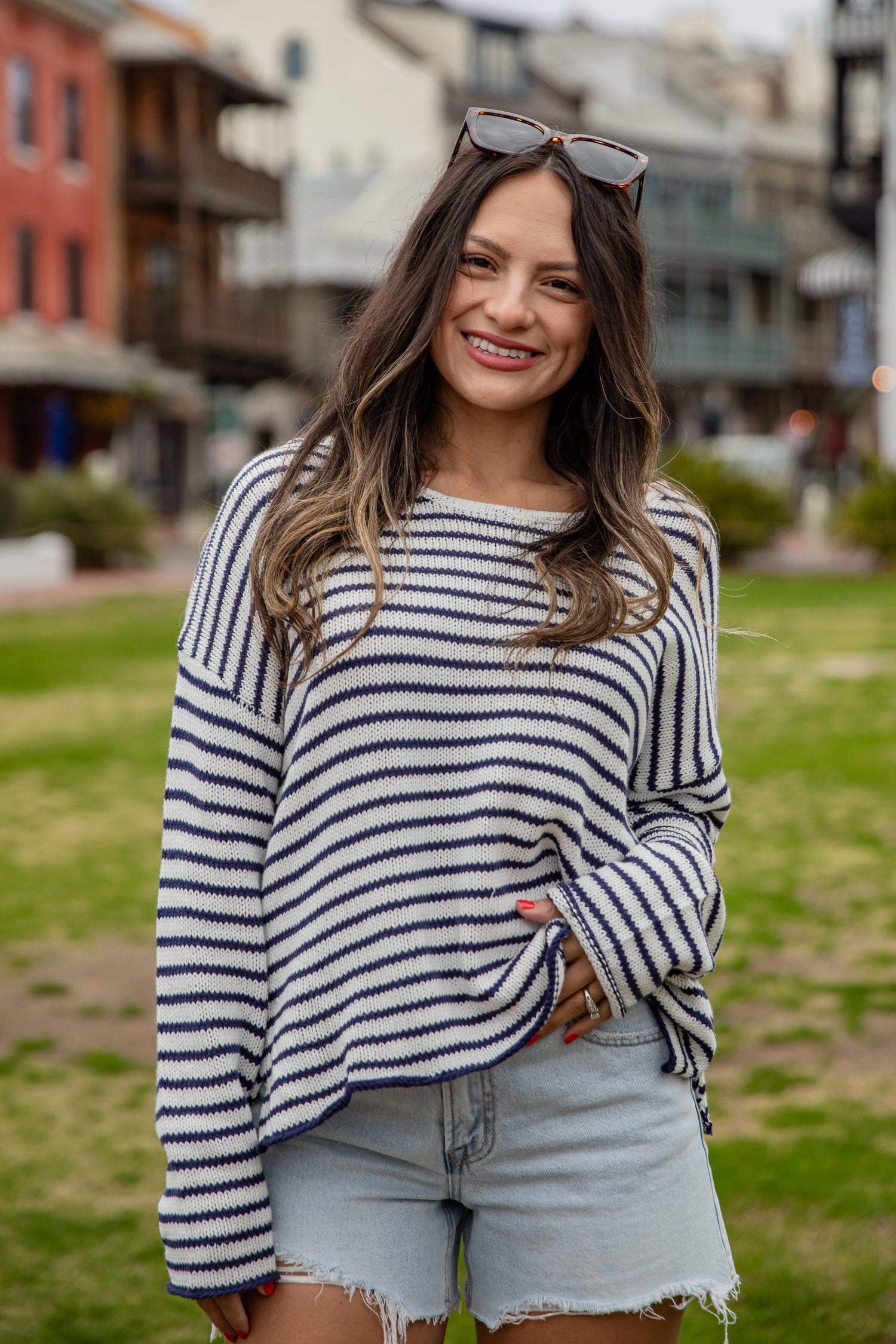 Woman wearing a striped sweater and denim shorts standing outdoors with buildings in the background