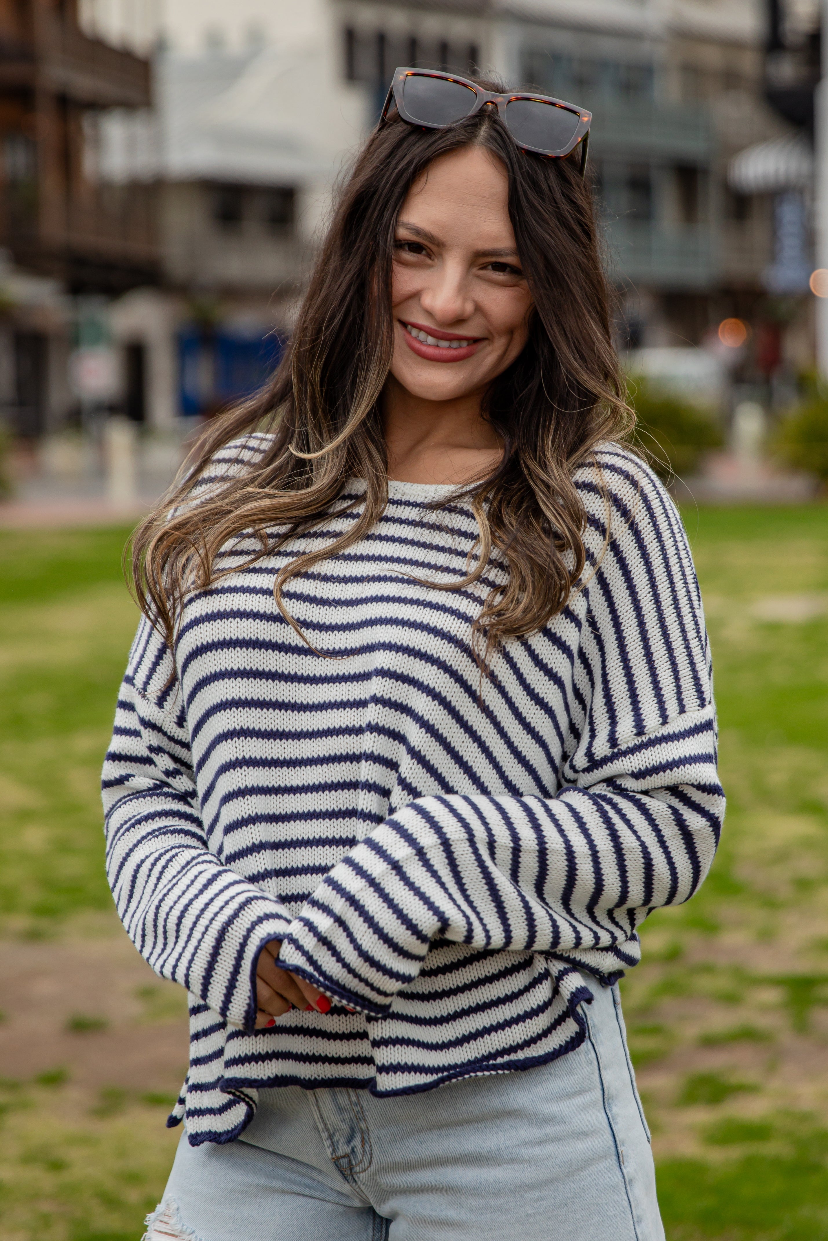 Woman wearing a striped sweater and sunglasses on her head, standing outdoors.