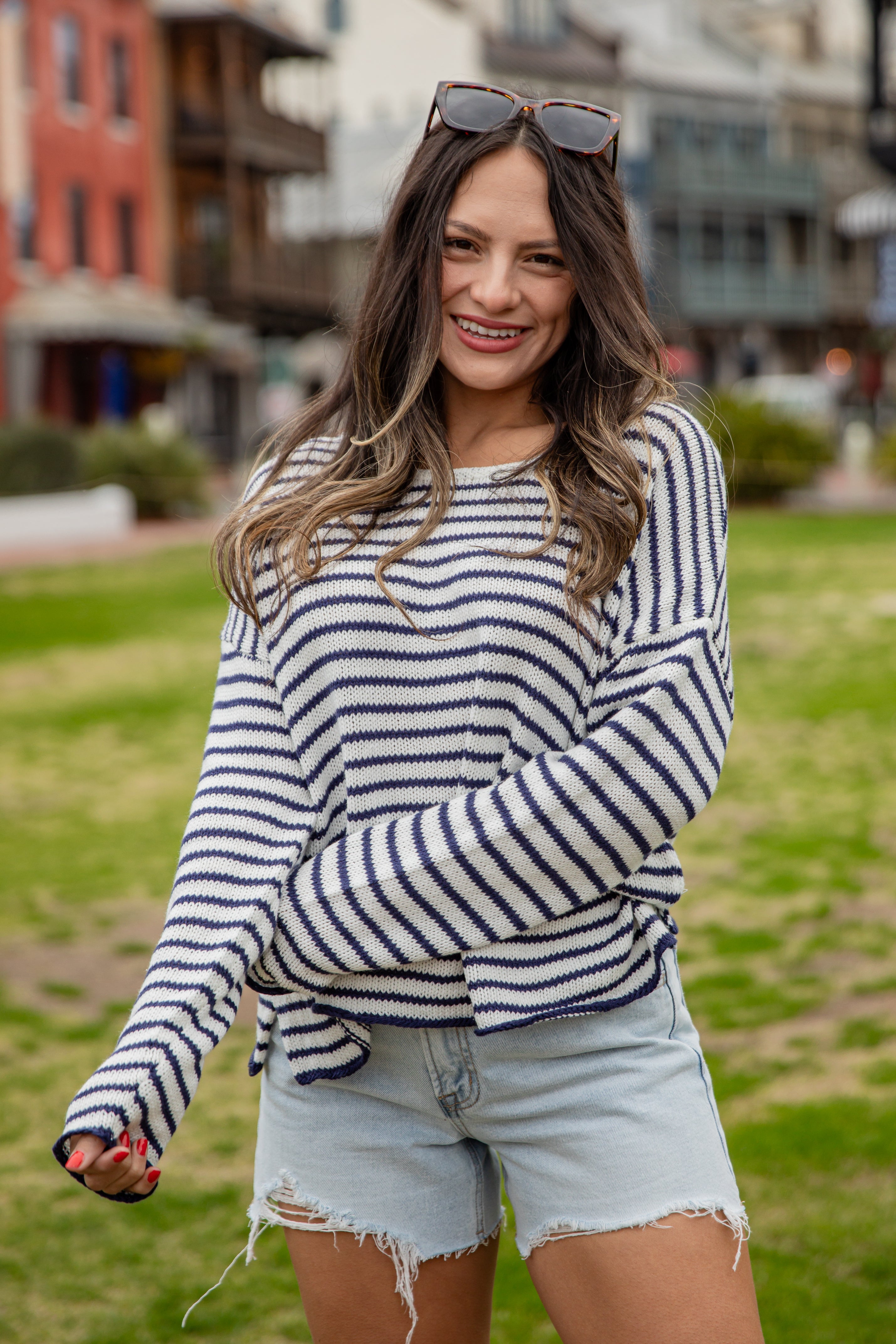 Woman wearing a striped sweater and denim shorts standing outdoors with buildings in the background