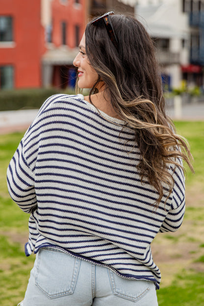 Woman wearing a striped sweater and light blue jeans outdoors with buildings in the background