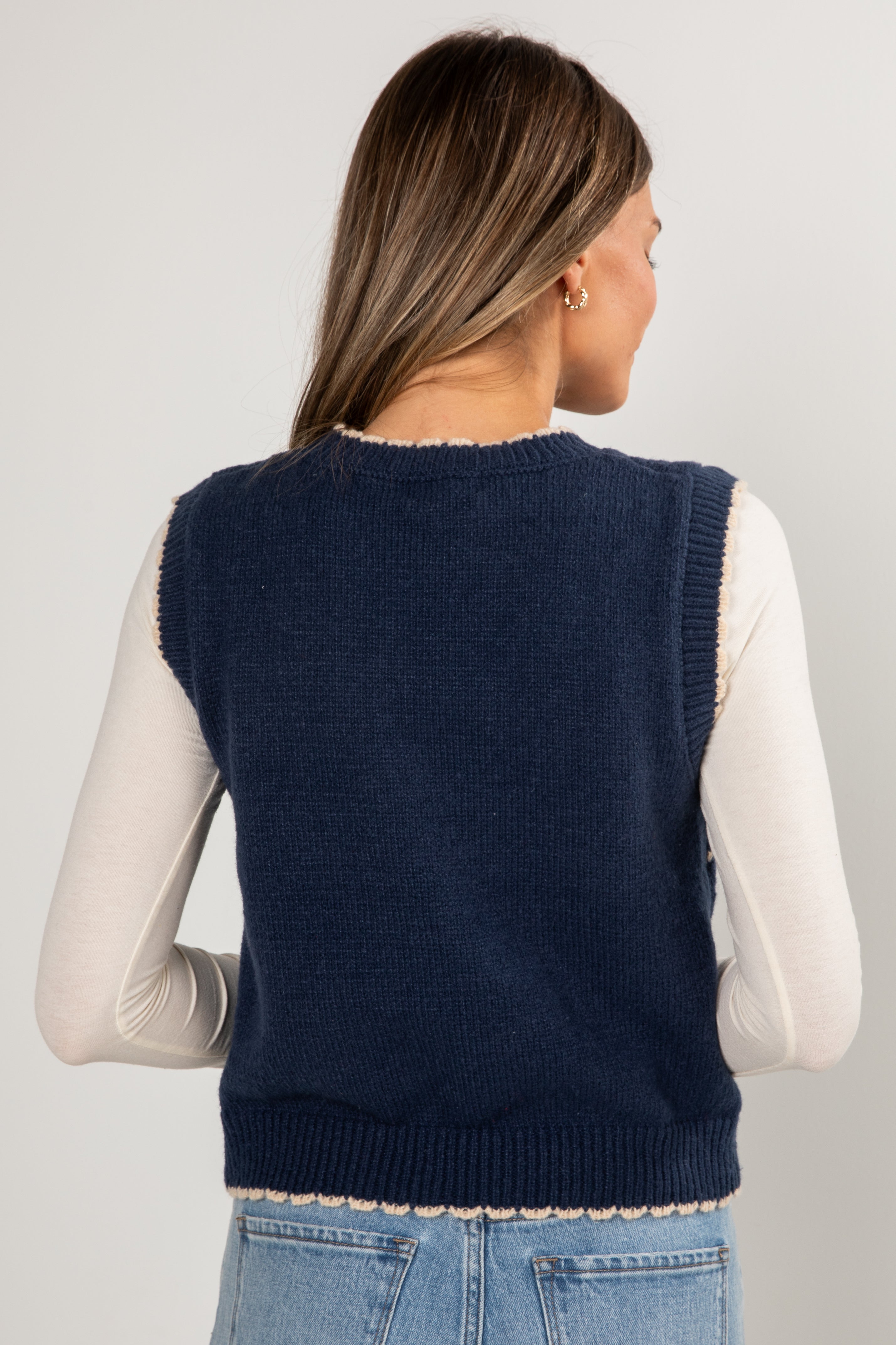 Woman wearing a navy blue knitted vest over a white long-sleeve shirt on a light gray background