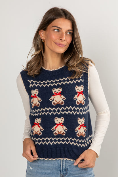Woman wearing a navy blue sweater vest with teddy bear patterns on a light gray background