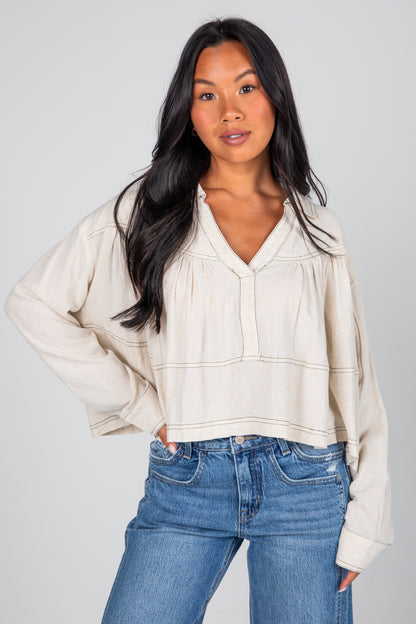Woman wearing a beige blouse and blue jeans against a gray background