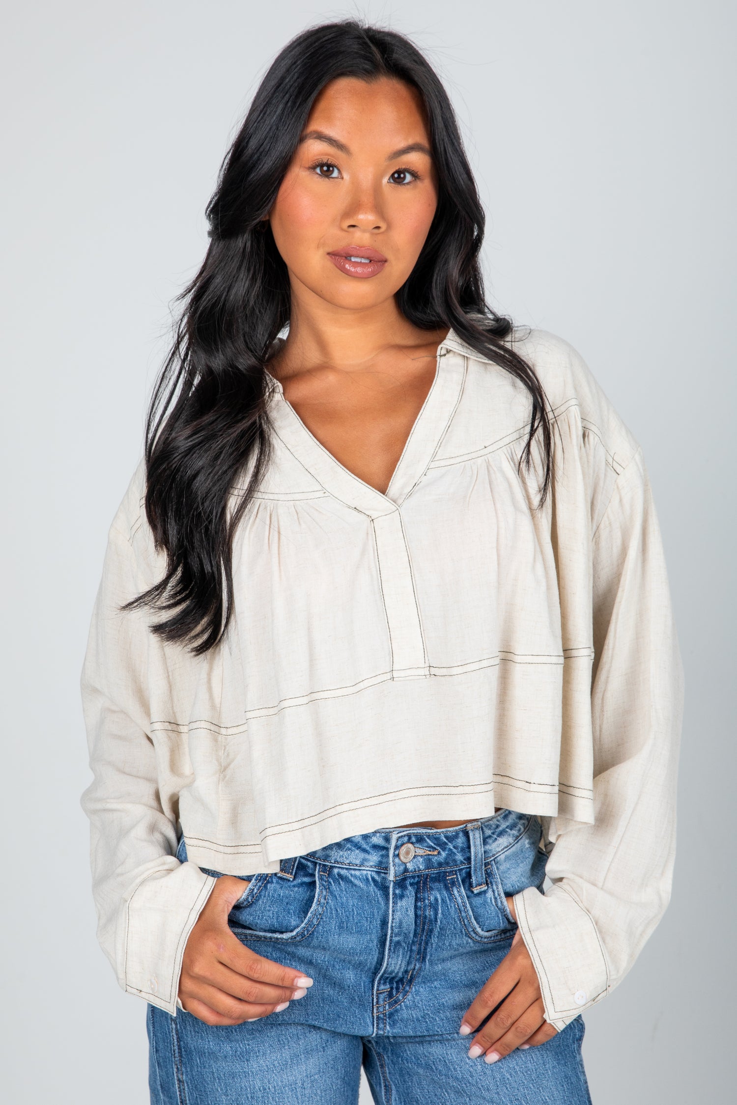 Woman wearing a beige blouse and blue jeans against a gray background