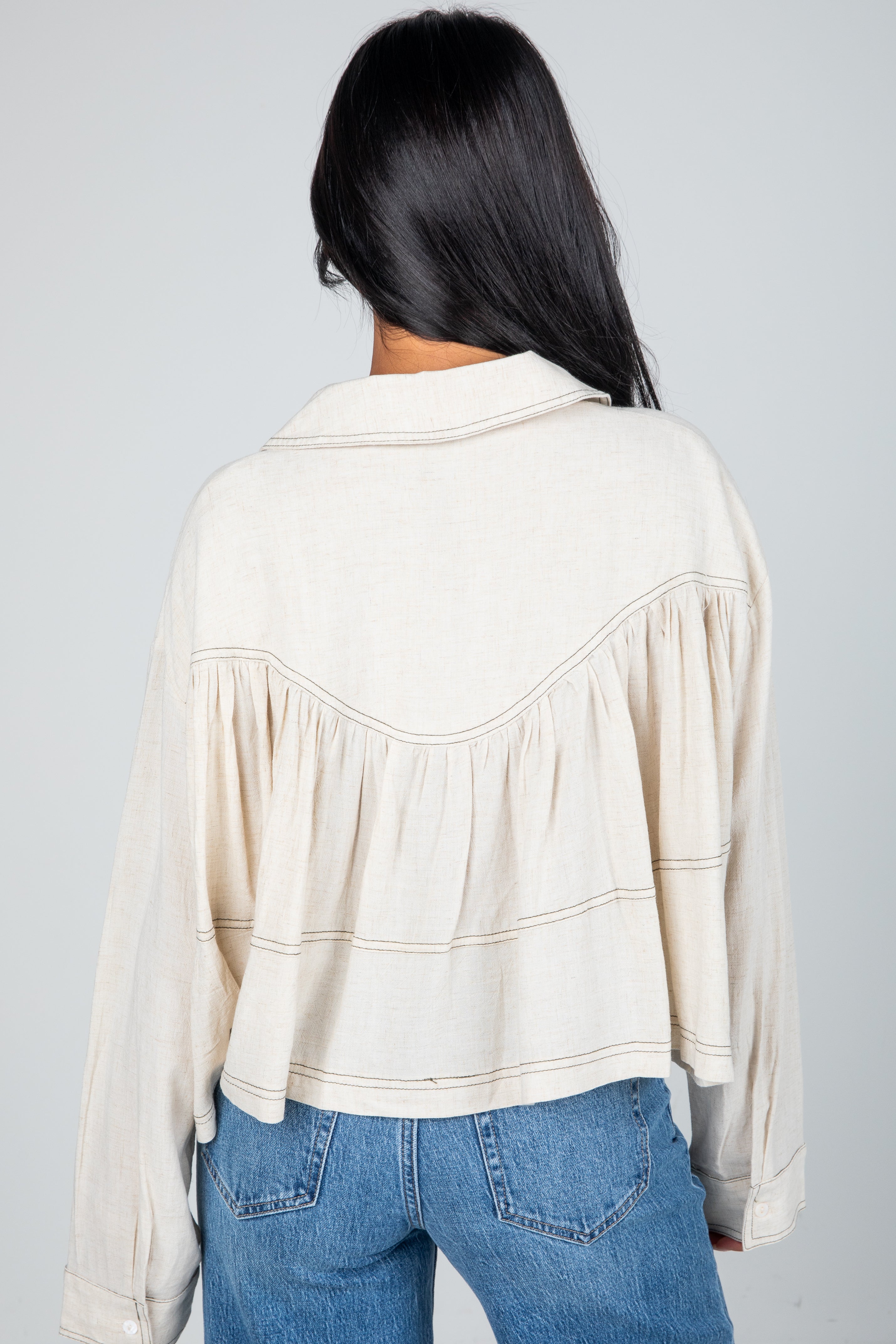 Person wearing a beige blouse with a subtle pattern and blue jeans on a gray background