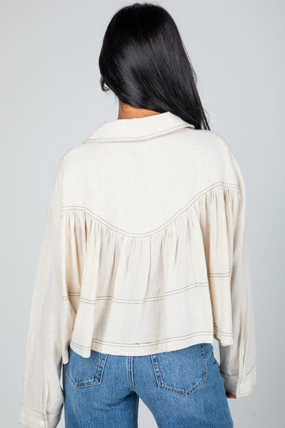 Person wearing a beige blouse with a subtle pattern and blue jeans on a gray background