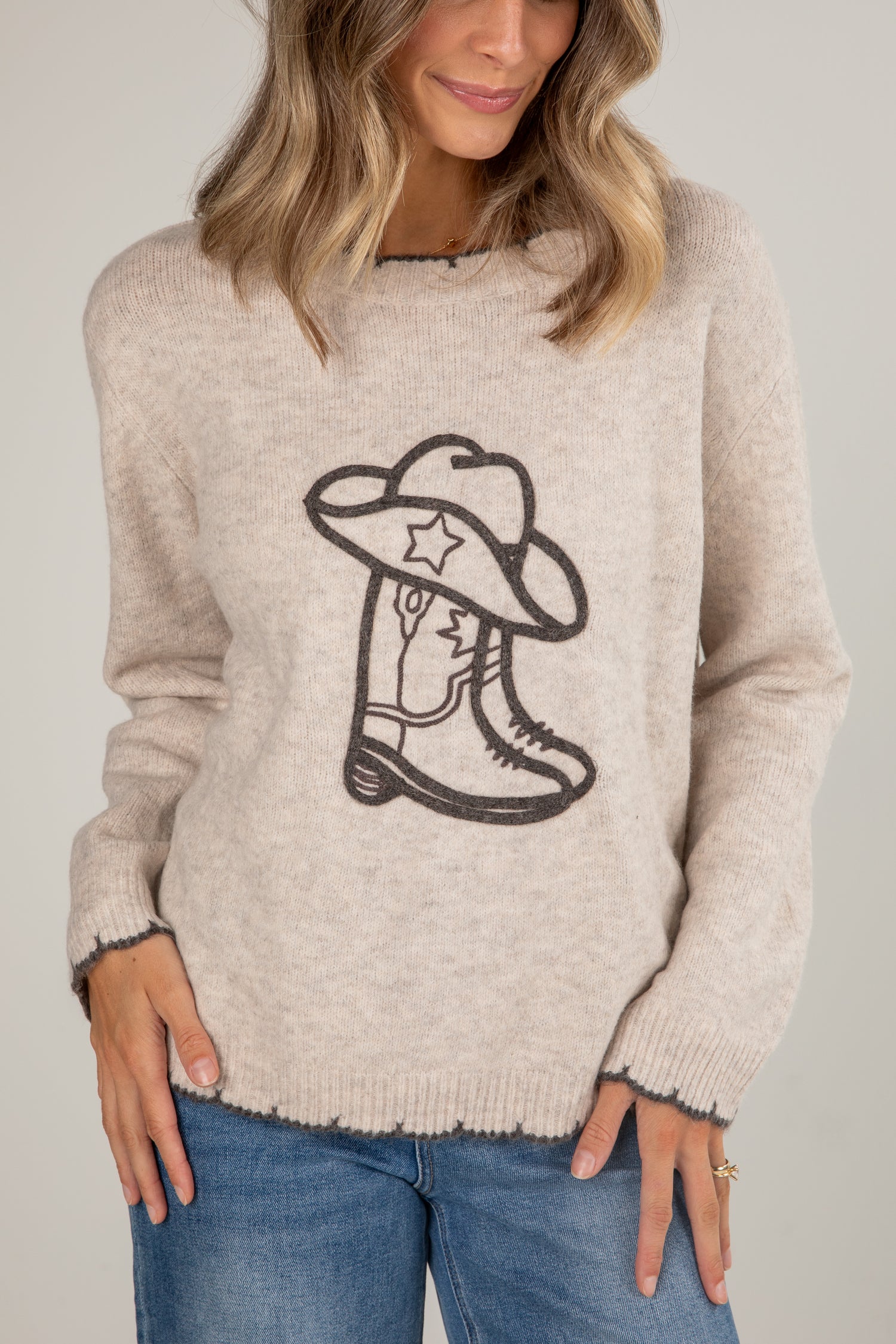 Person wearing a beige sweater with a cowboy boot and hat design on a plain background
