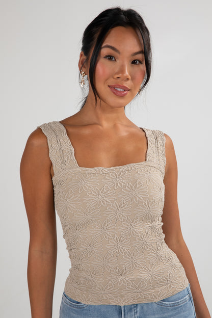 Woman wearing a beige patterned tank top against a plain background