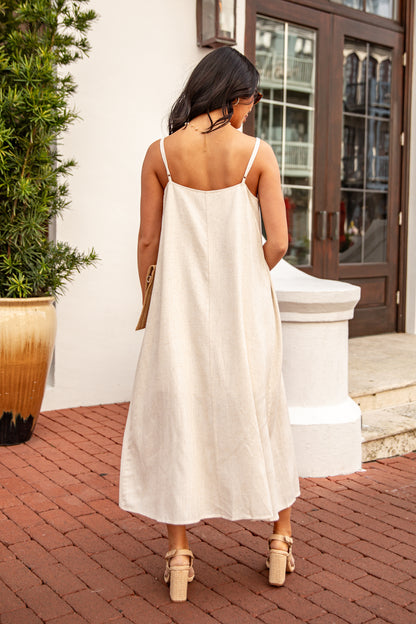 Woman in a white dress standing on a brick patio with a plant and door in the background