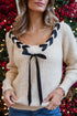 Person wearing a beige sweater with black ribbon details against a festive background.