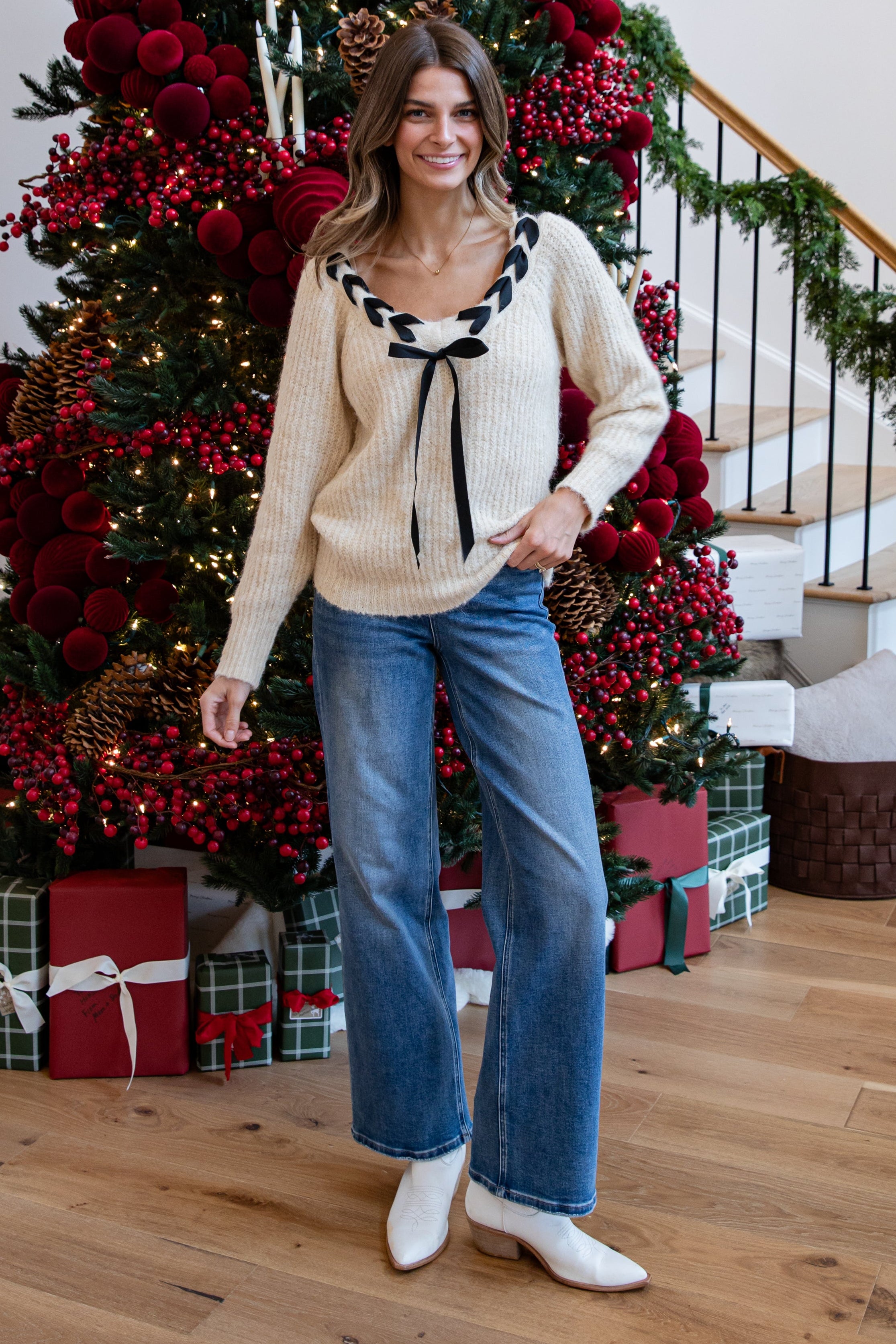 Woman standing in front of a decorated Christmas tree with presents underneath.