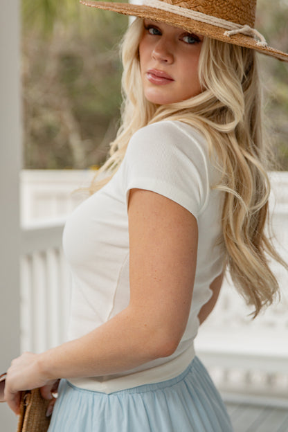 Woman wearing a white top and light blue skirt with a straw hat outdoors.