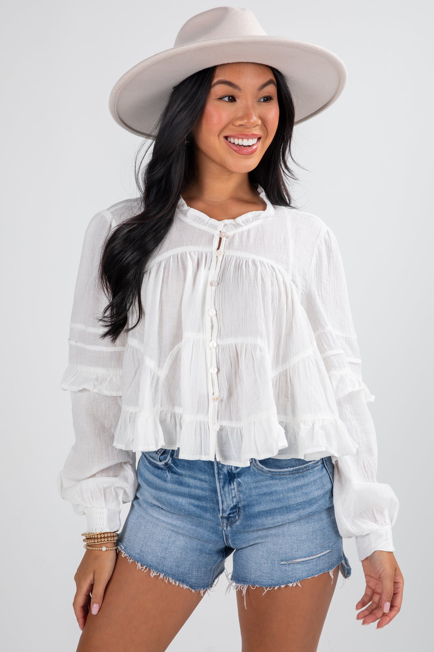 Woman wearing a white blouse with ruffled details and denim shorts on a plain background