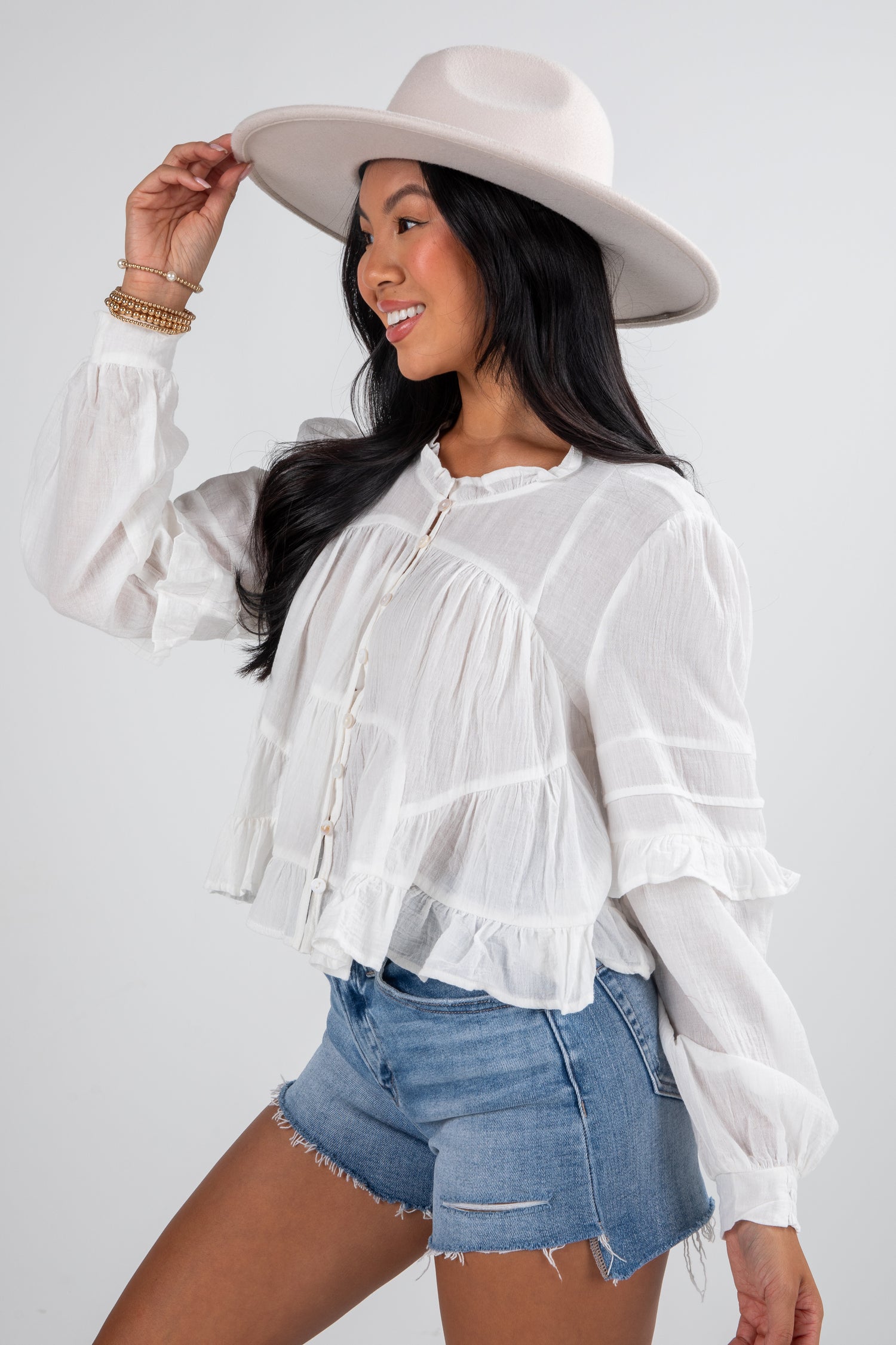 Woman wearing a white blouse, denim shorts, and a beige hat on a plain background