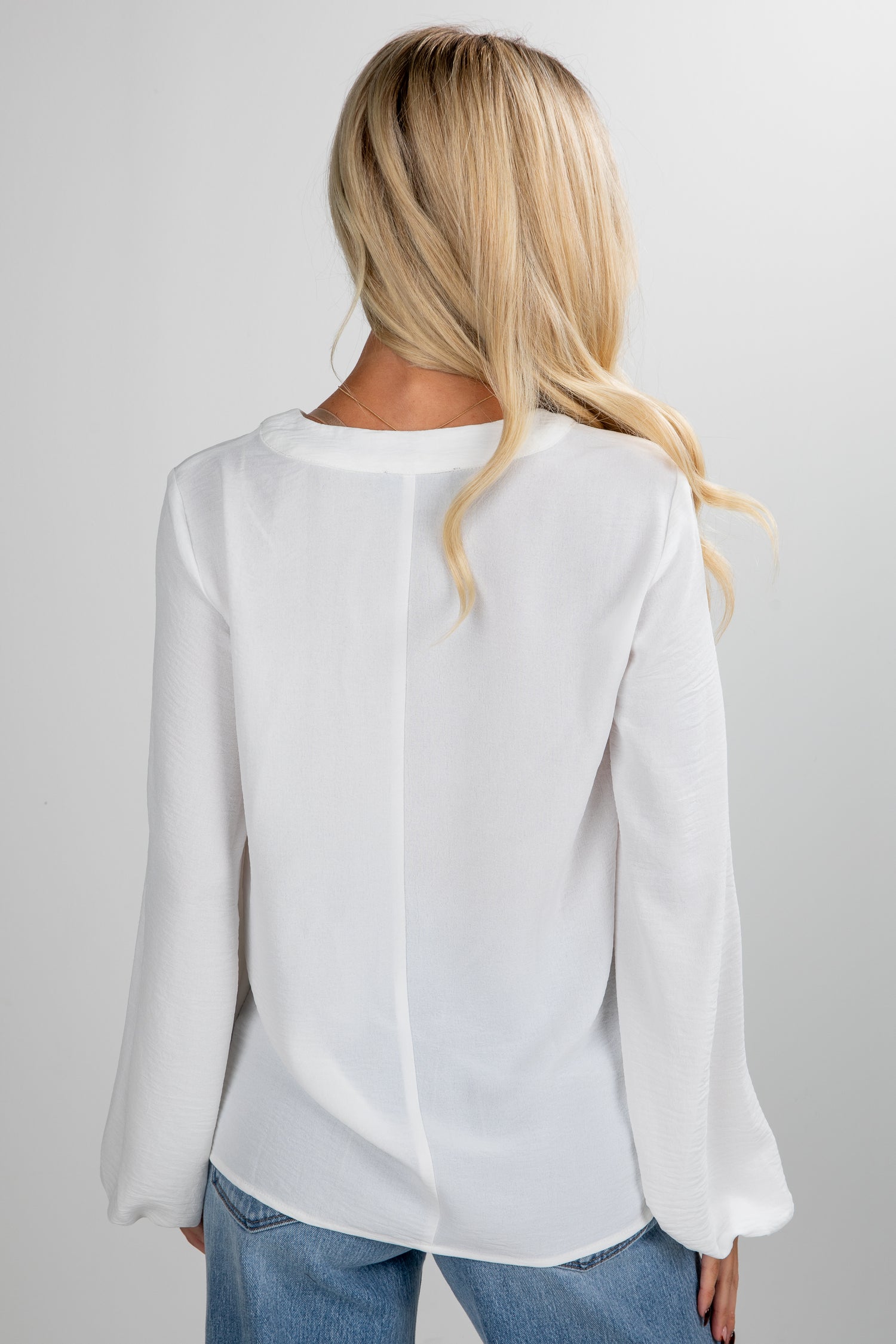 Person wearing a white blouse and blue jeans on a plain background