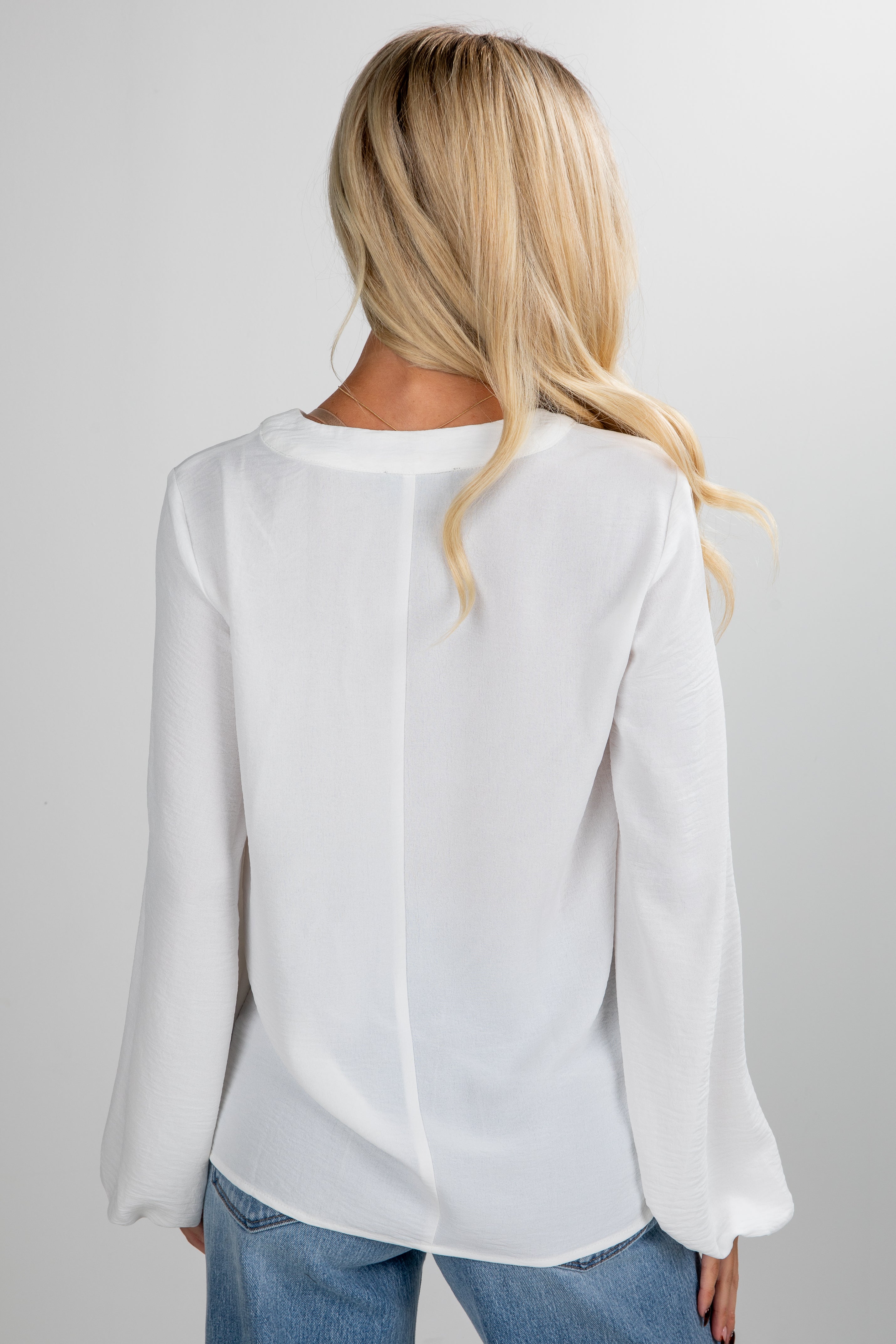 Person wearing a white blouse and blue jeans on a plain background