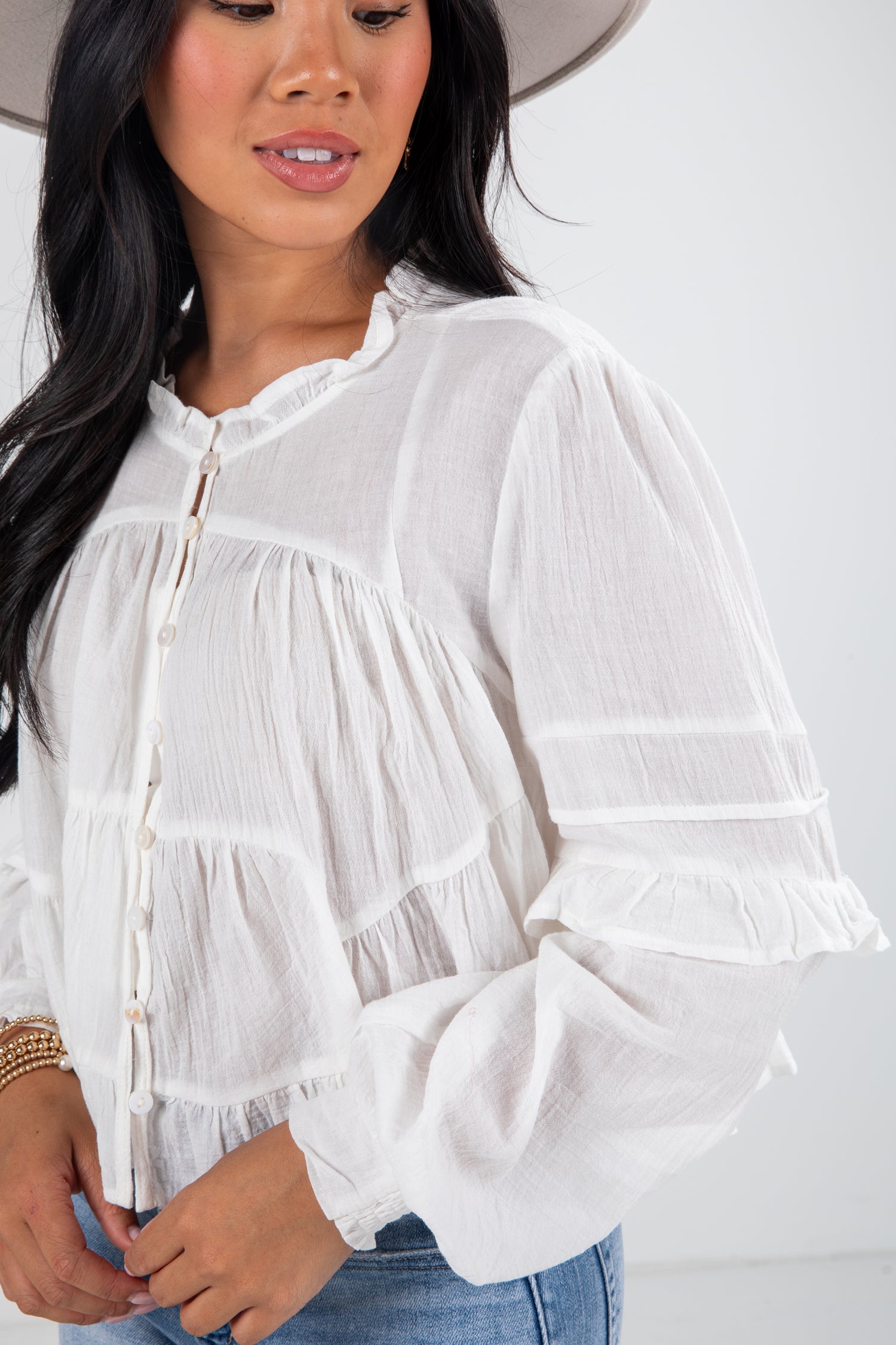 Woman wearing a white blouse with ruffled details on a plain background