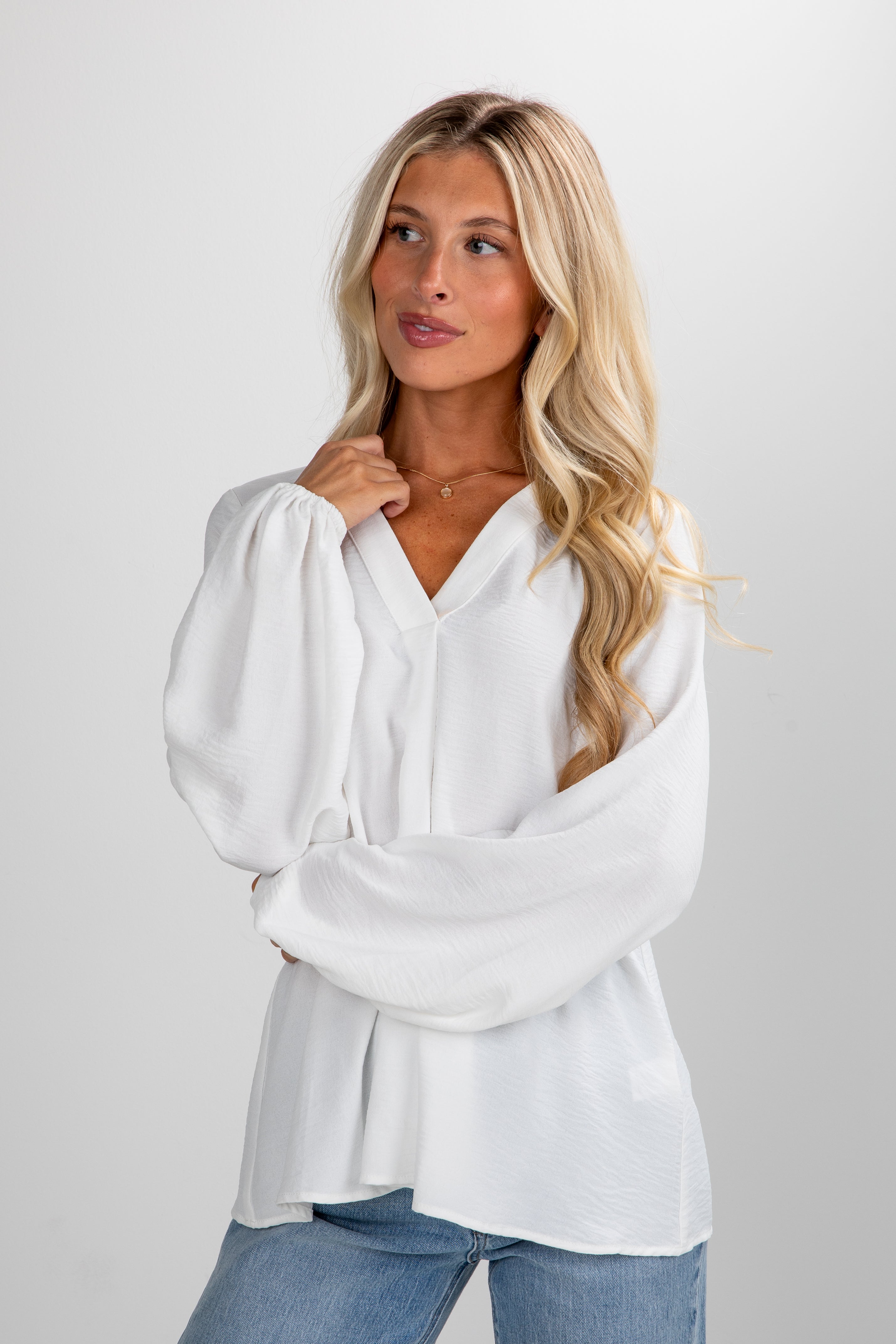 Woman wearing a white blouse and blue jeans on a plain background