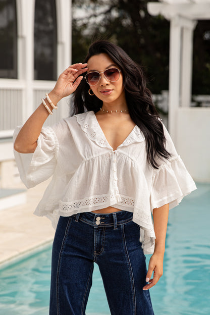 Woman wearing a white blouse and blue jeans by a pool