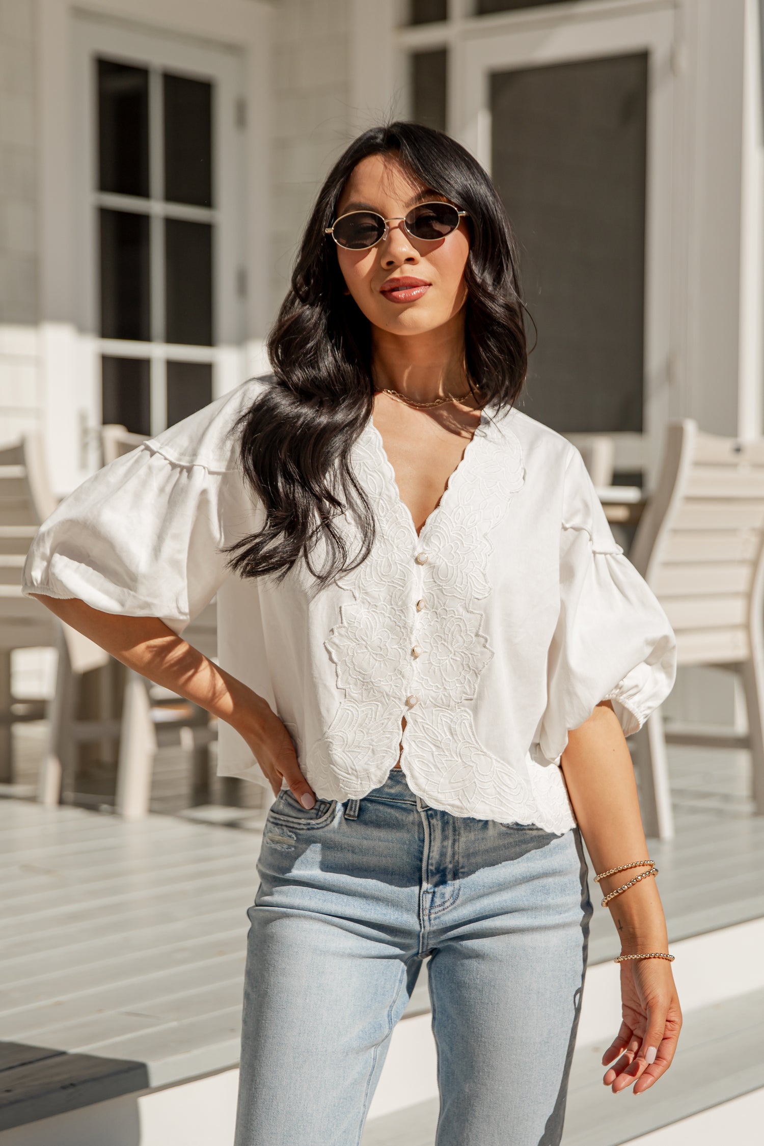 Woman wearing a white blouse and light blue jeans standing outdoors.