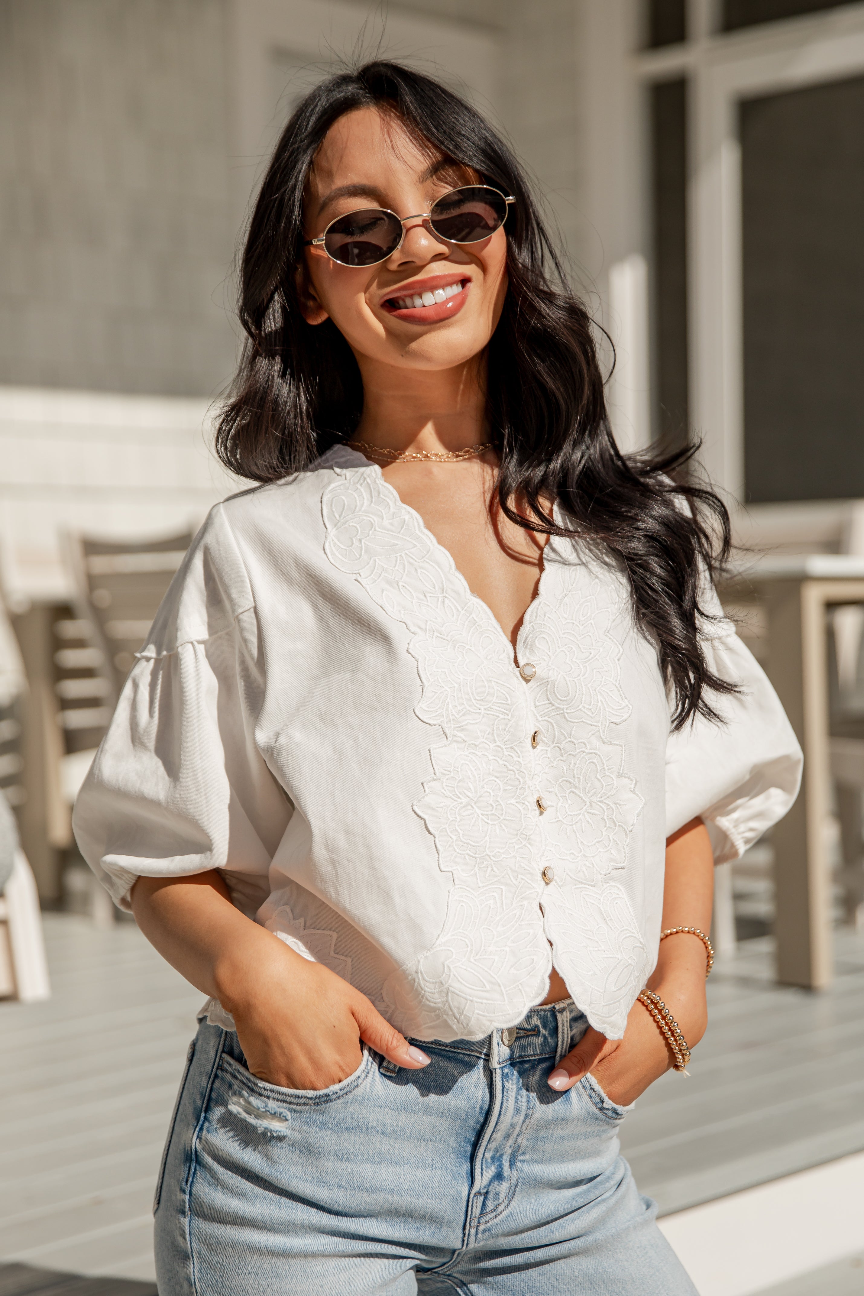 Woman wearing a white blouse and blue jeans with sunglasses outdoors.