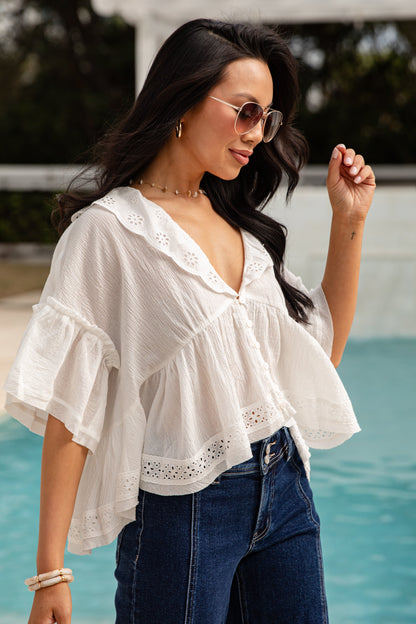 Woman wearing a white blouse with ruffled sleeves and blue jeans by a pool.