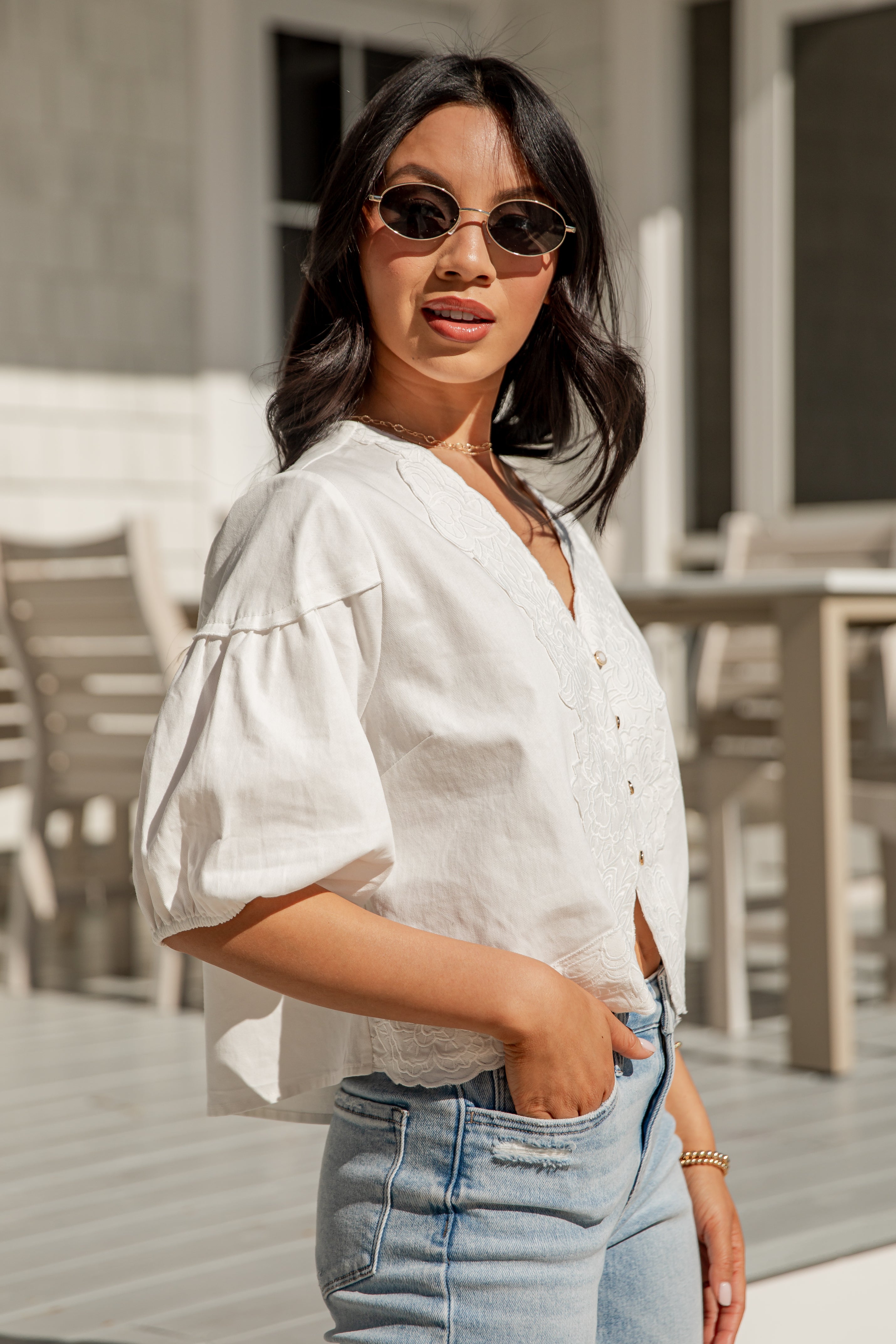 Woman wearing a white blouse and blue jeans with sunglasses outdoors.