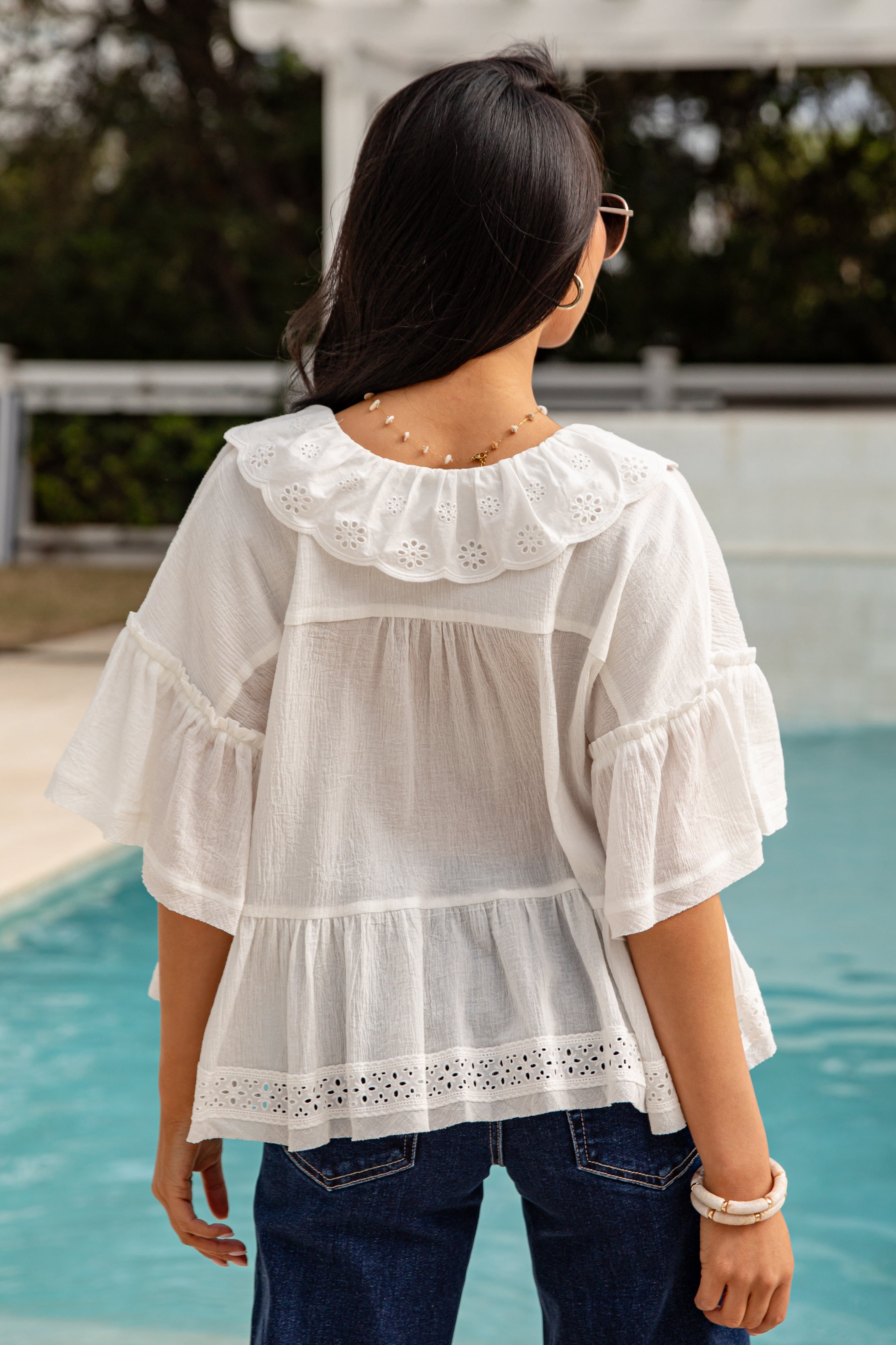 Woman wearing a white blouse with ruffled sleeves and collar by a pool.