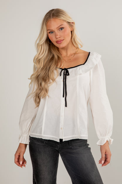 Woman wearing a white blouse with black trim against a plain background