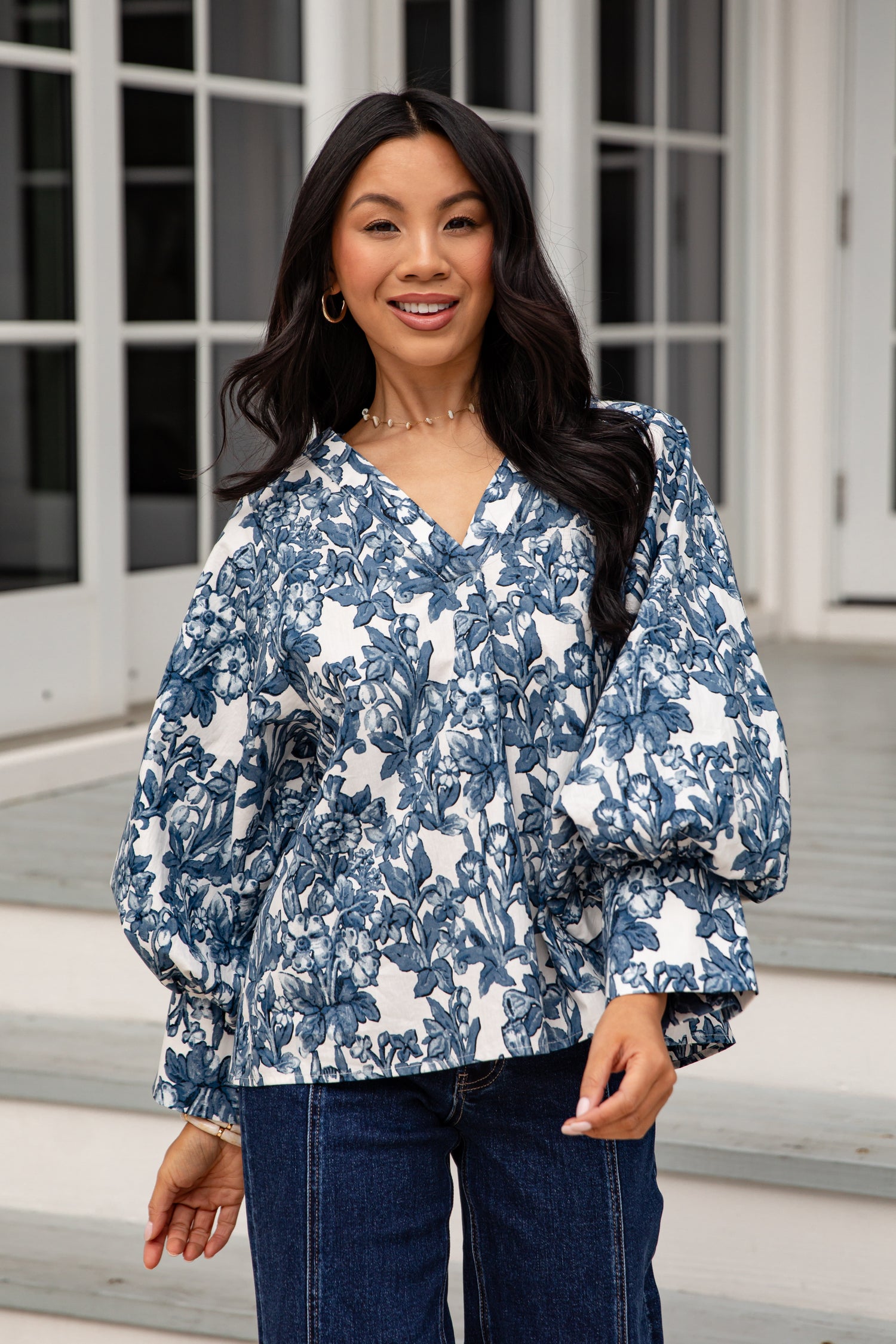Woman wearing a blue floral blouse and jeans standing outdoors.