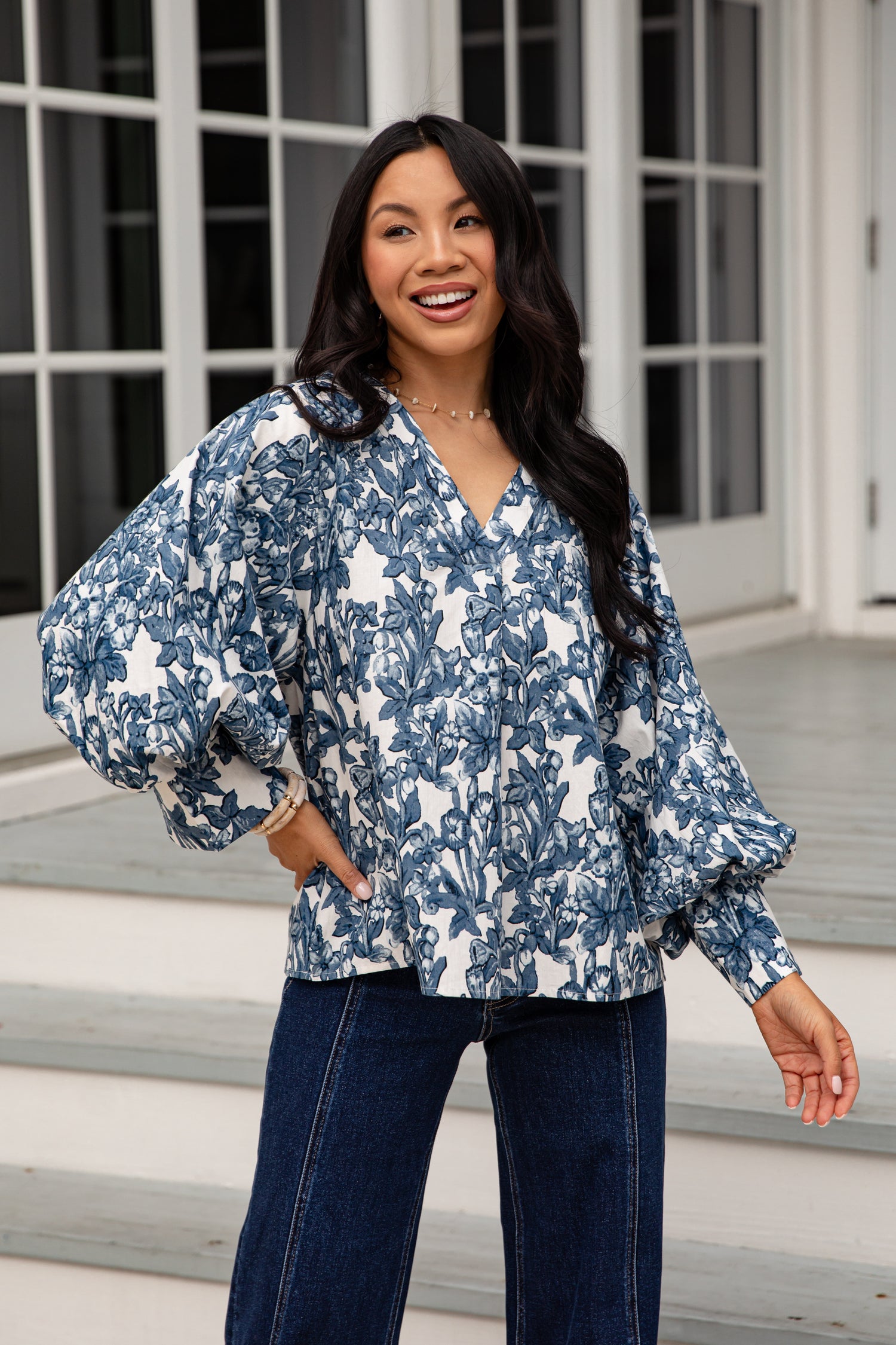 Woman wearing a blue floral blouse and jeans standing on steps.