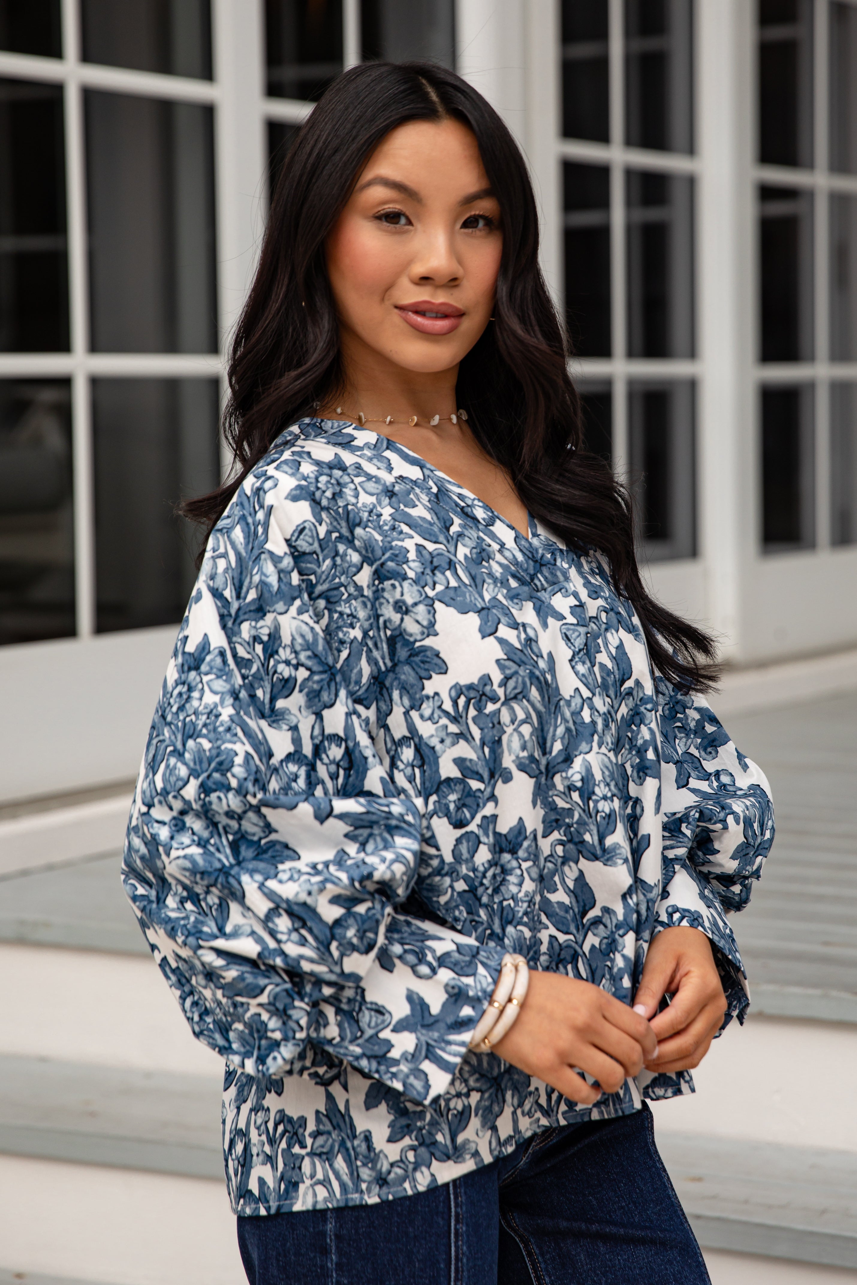 Woman wearing a blue and white floral blouse standing in front of a window.