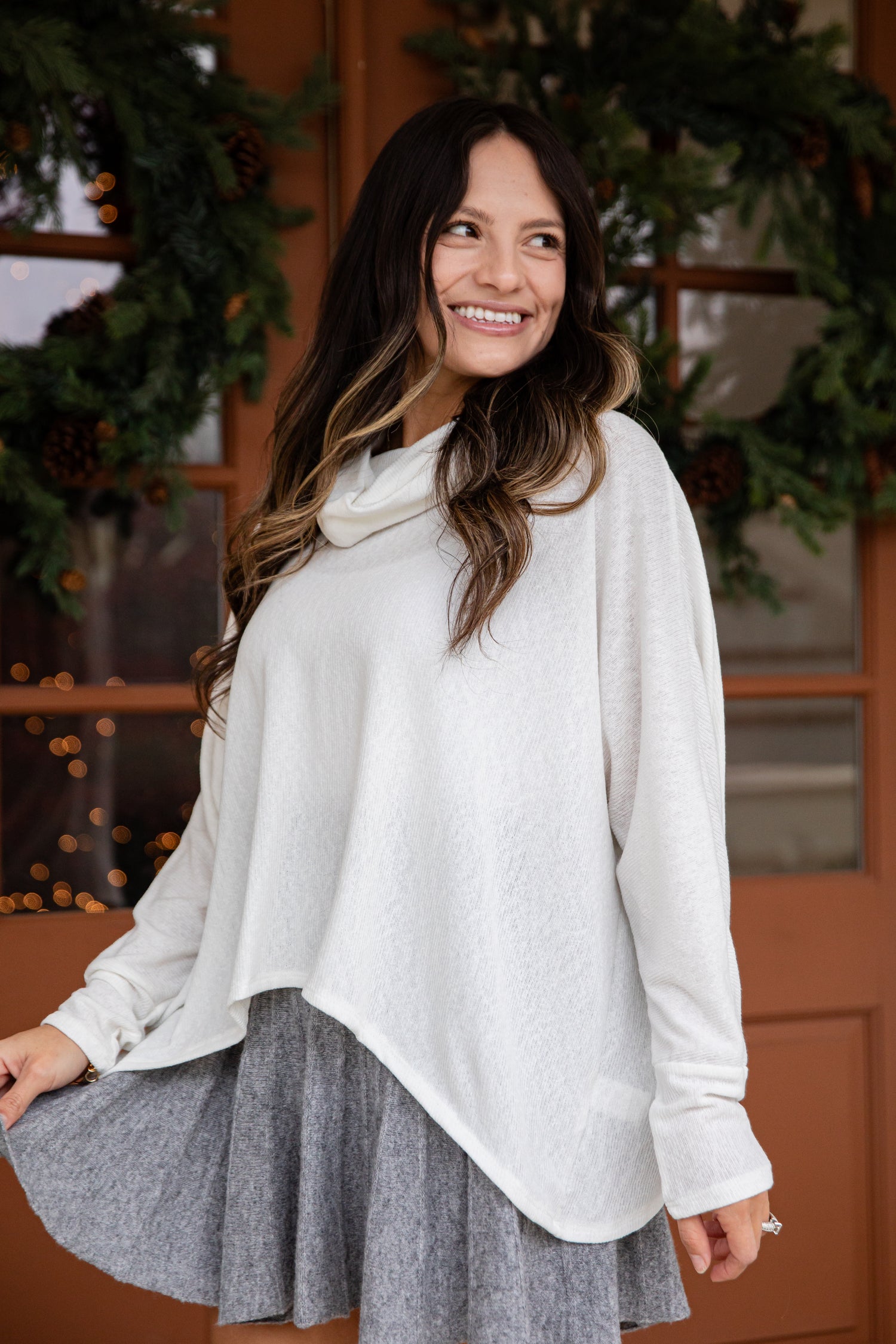 Woman wearing a white blouse and gray skirt standing in front of a decorated door.