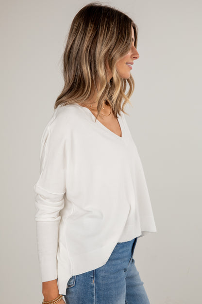 Woman wearing a white long-sleeve top and blue jeans against a plain background