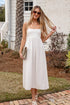 Woman in a white dress standing on a brick path in front of a house.