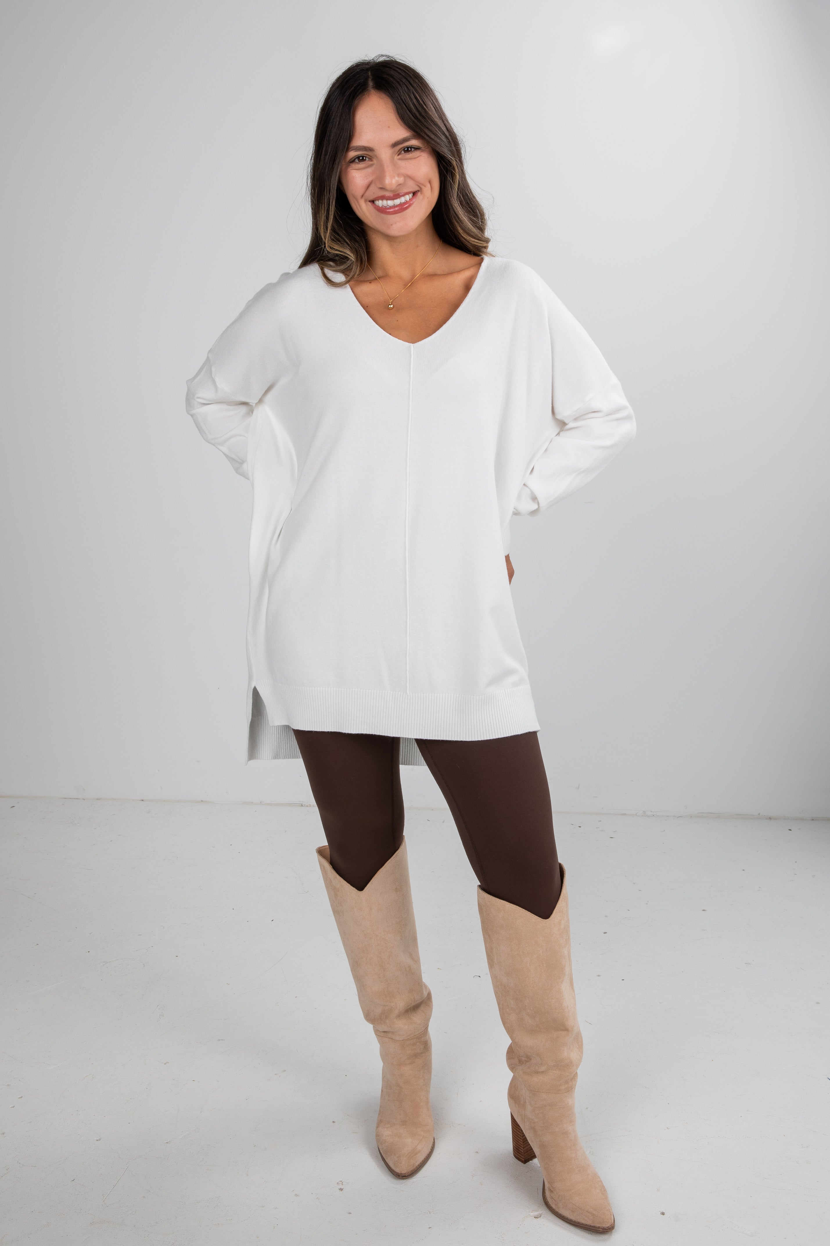 Woman wearing a white long-sleeve top and brown pants with beige knee-high boots on a white background