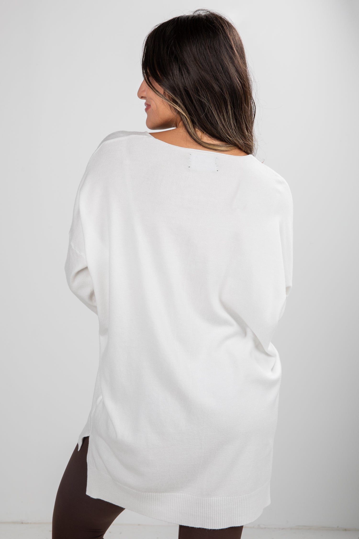 Woman wearing a white oversized sweater against a plain background