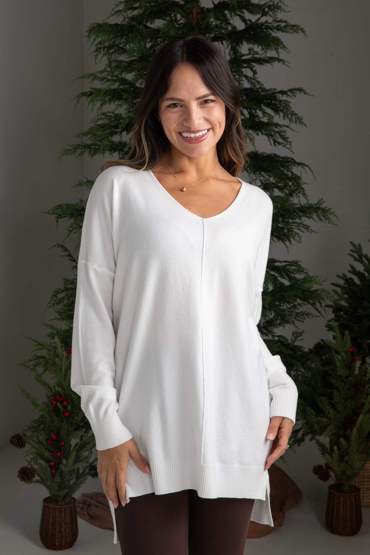 Woman wearing a white long-sleeve top in front of decorative plants.