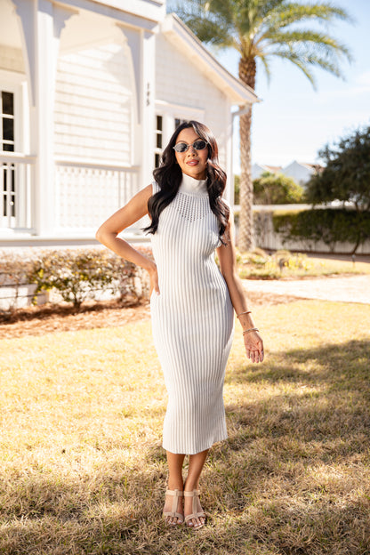 Woman in a white ribbed dress standing outdoors with a house and palm tree in the background.