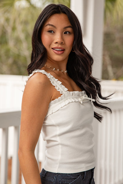 Woman wearing a white top with lace details on a blurred outdoor background