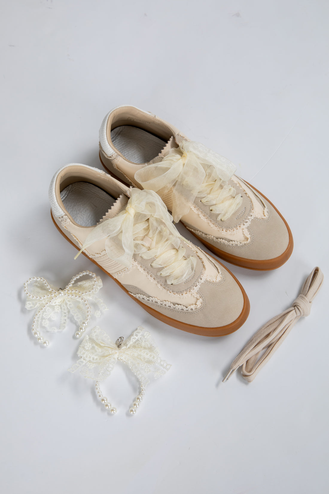 Pair of cream-colored shoes with lace details on a light gray background