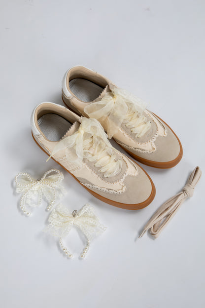 Pair of cream-colored shoes with lace details on a light gray background