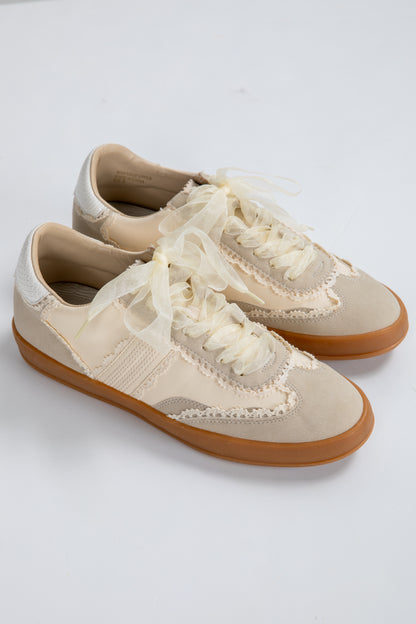 Pair of beige sneakers with white laces on a light gray background