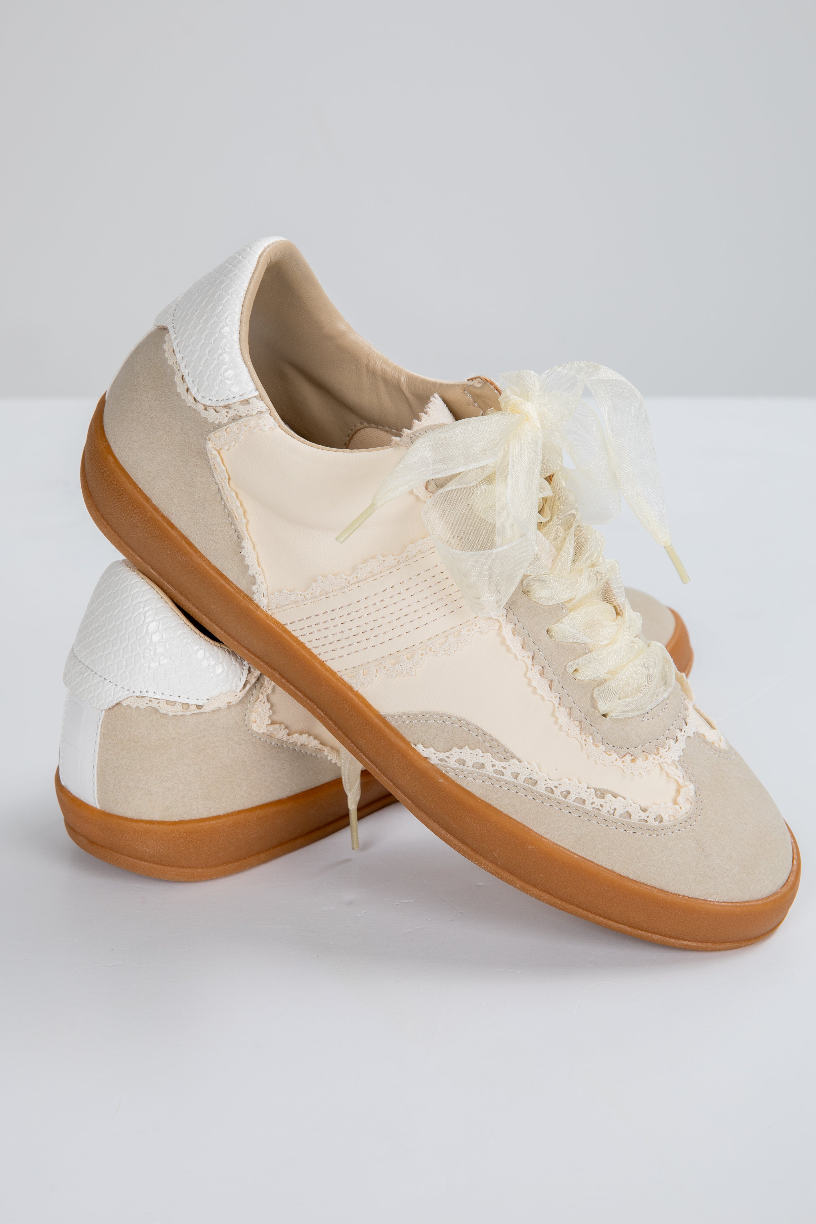 Pair of beige sneakers with white laces on a light gray background