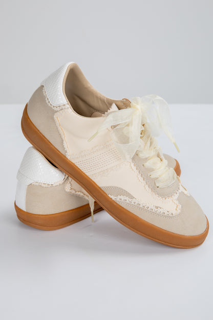 Pair of beige sneakers with white laces on a light gray background
