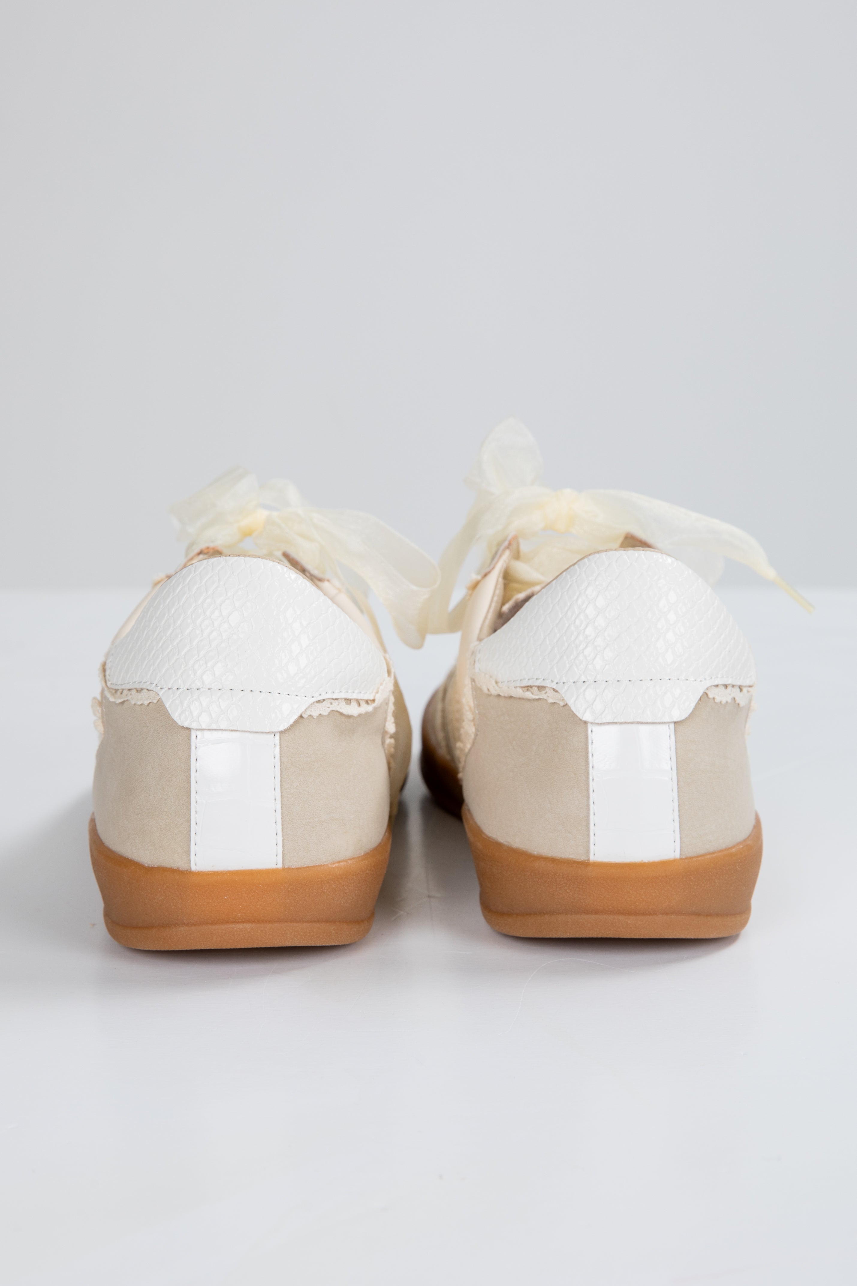 Pair of white shoes with brown soles on a light gray background