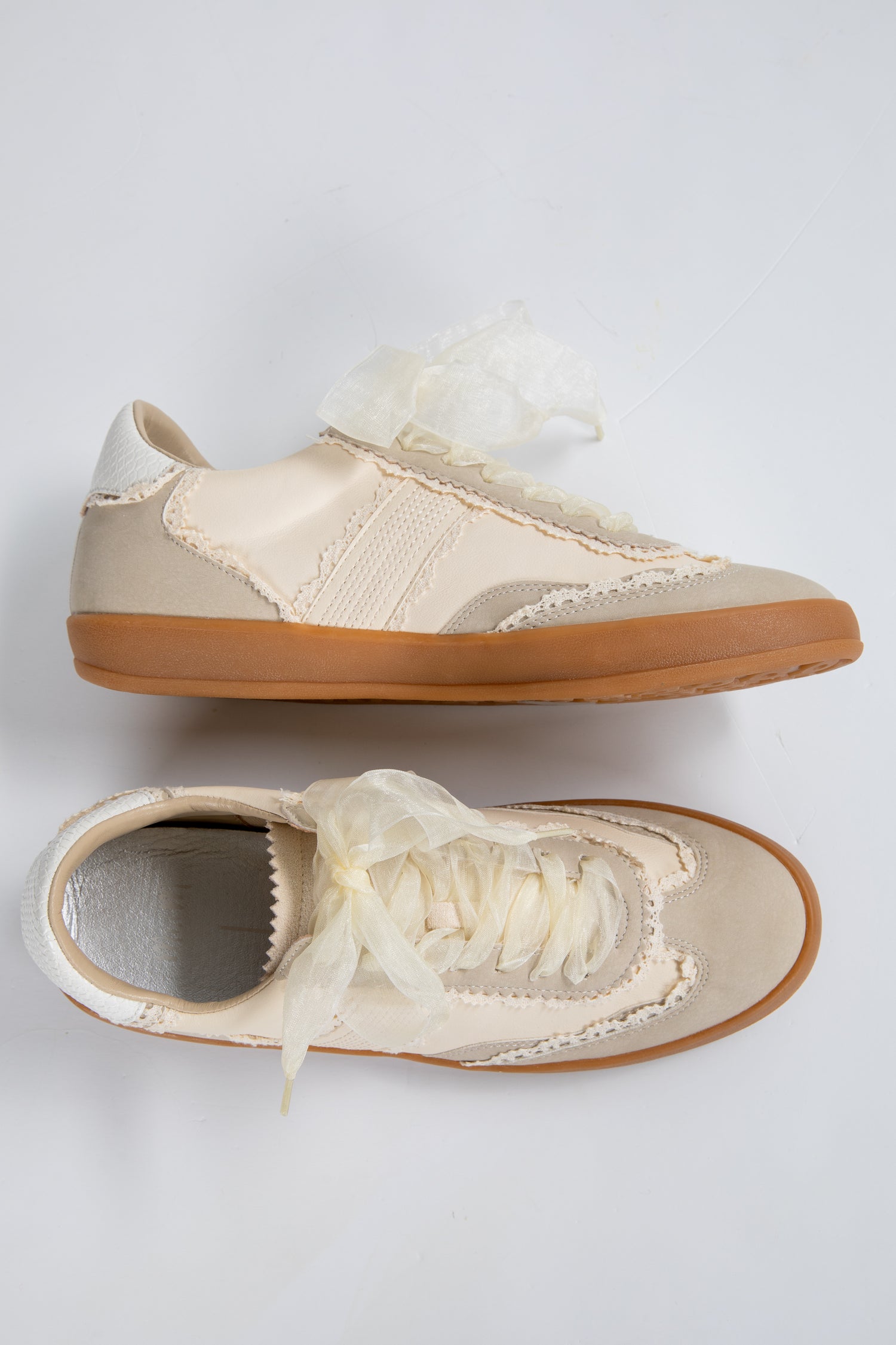 Pair of beige sneakers with white laces on a light gray background
