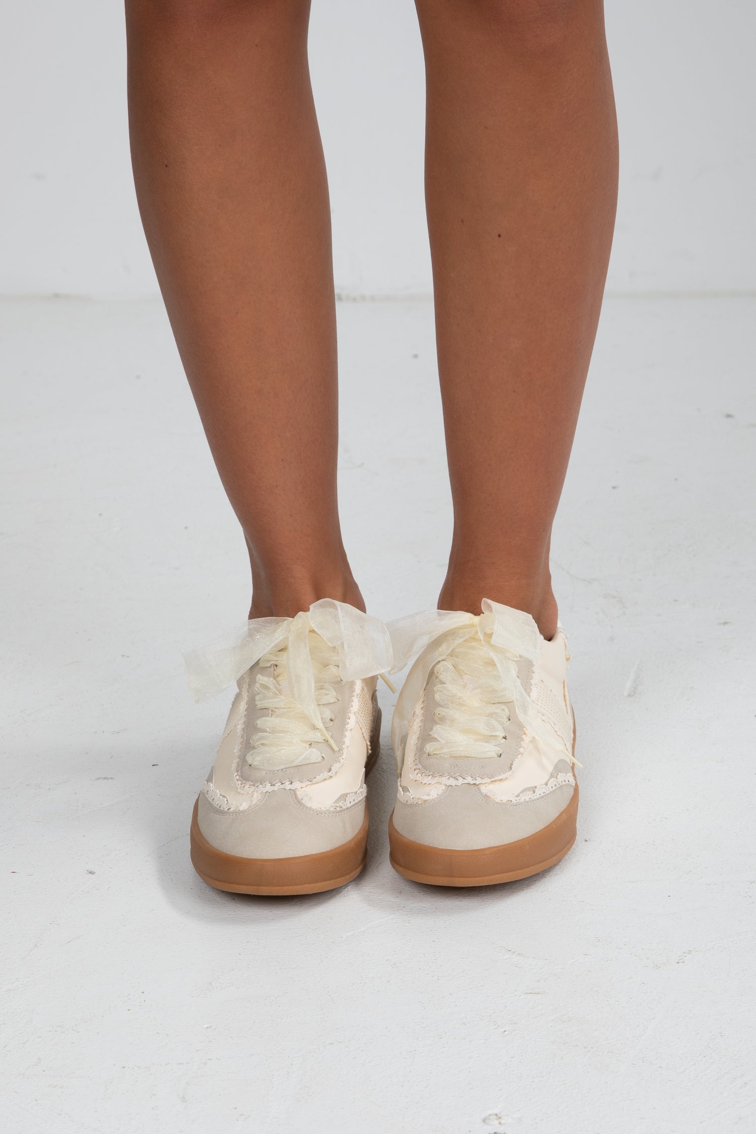 Beige sneakers with brown soles worn by a person on a white background