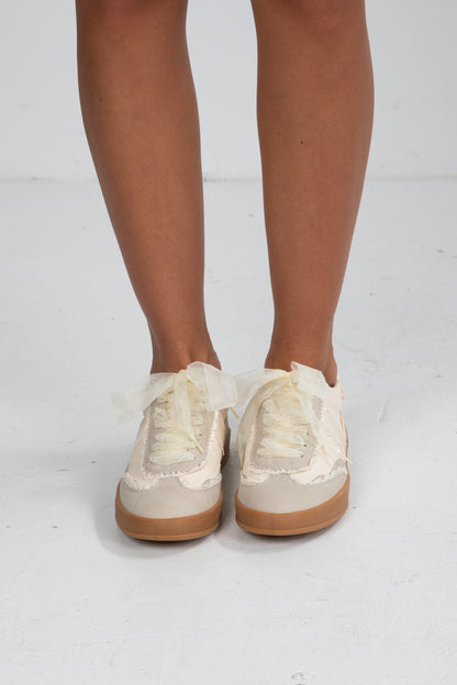 Beige sneakers with brown soles worn by a person on a white background