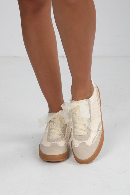White sneakers with brown soles worn by a person on a white background